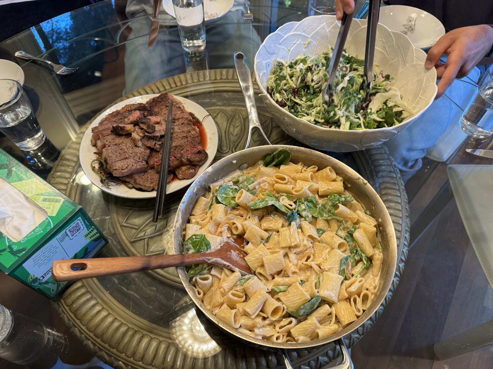 A shared dinner of pasta, steak, and salad being served at the table